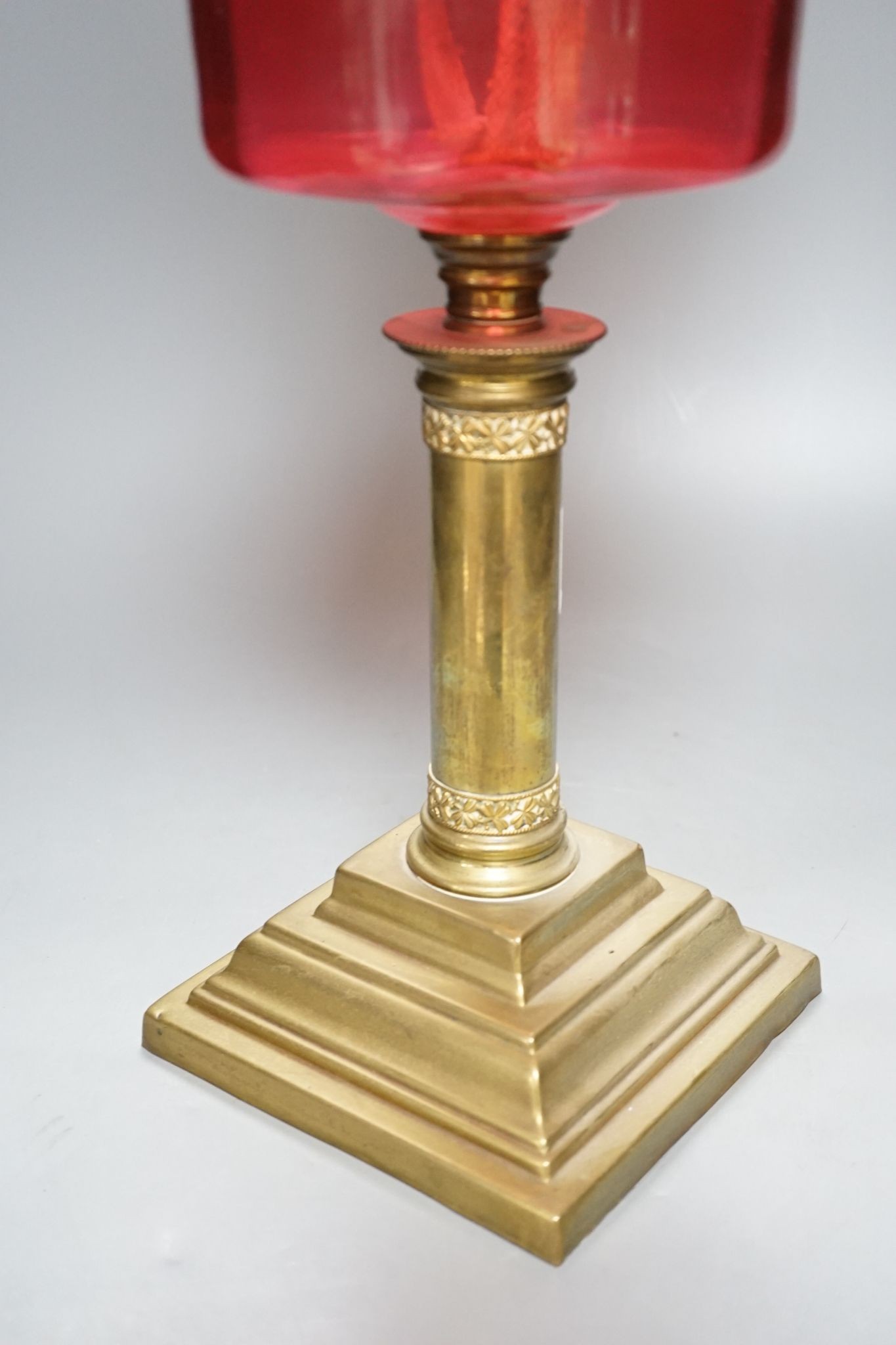 A brass and cranberry glass oil lamp with shade and chimney, total height 66cm